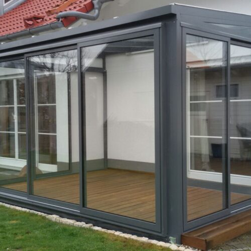 Ein Sommergarten / Wintergarten mit Glaswänden und grauen Metallrahmen an einem Haus